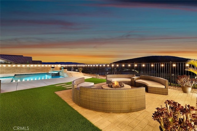 pool at dusk featuring a pool with connected hot tub, an outdoor living space with a fire pit, and a lawn