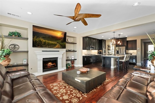 living area featuring baseboards, visible vents, dark wood-style floors, a lit fireplace, and built in shelves