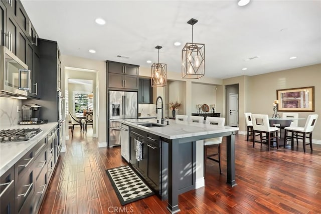 kitchen featuring dark wood finished floors, stainless steel appliances, backsplash, a sink, and a kitchen breakfast bar