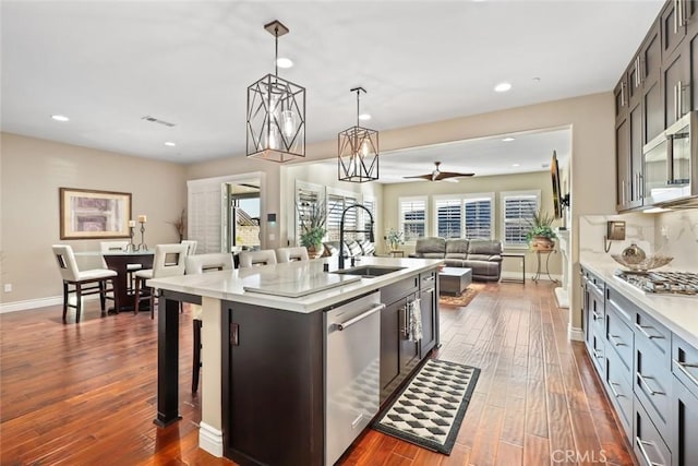 kitchen with dark wood-style floors, stainless steel appliances, light countertops, a kitchen island with sink, and a sink