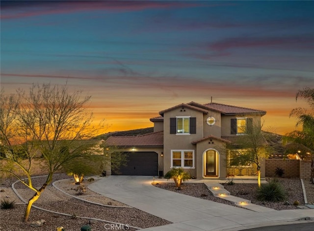 mediterranean / spanish-style home with a garage, concrete driveway, a tile roof, and stucco siding