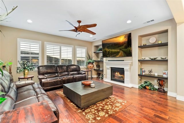 living room featuring visible vents, baseboards, built in features, hardwood / wood-style floors, and a glass covered fireplace