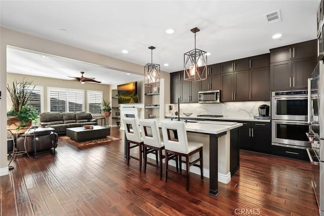 kitchen featuring dark wood-style floors, a breakfast bar, decorative light fixtures, stainless steel appliances, and light countertops