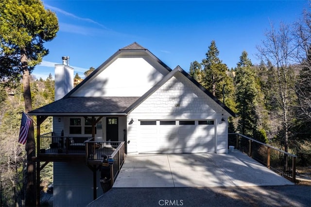 view of front of house featuring driveway, a shingled roof, a chimney, and an attached garage