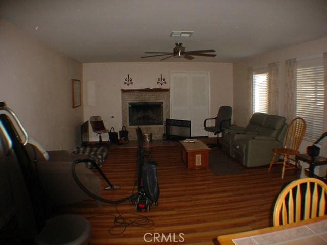 living room with visible vents, ceiling fan, a tiled fireplace, and wood finished floors