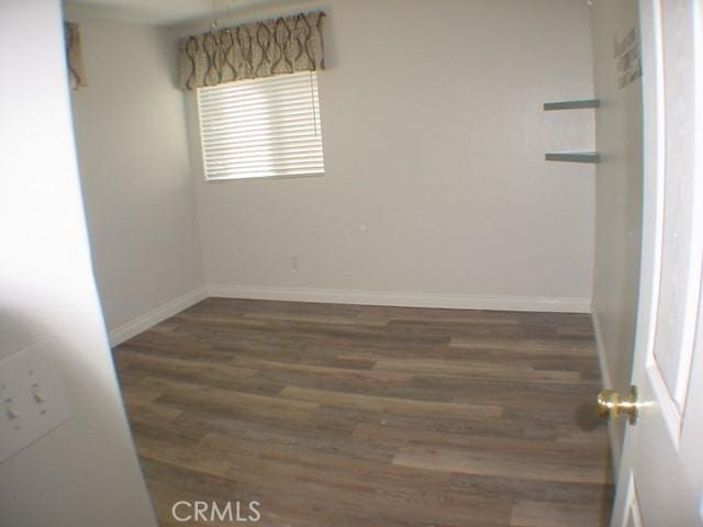 spare room with dark wood-type flooring and baseboards