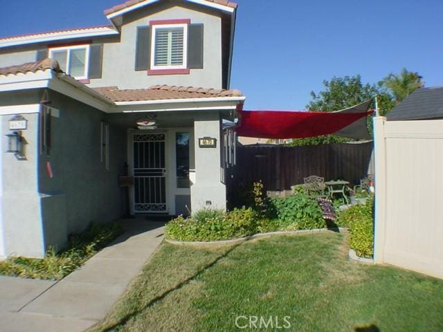 doorway to property with a tiled roof, fence, a lawn, and stucco siding