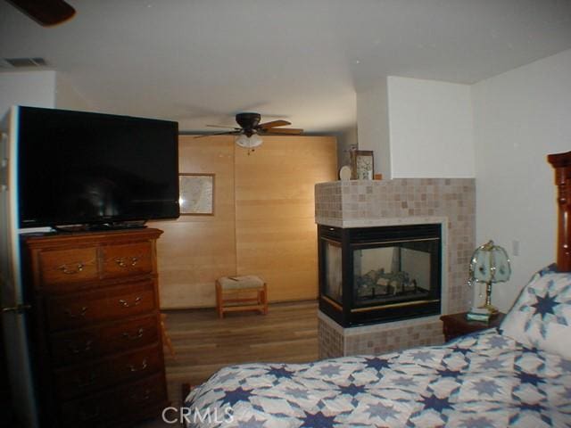 bedroom with dark wood-style floors, ceiling fan, visible vents, and a tile fireplace