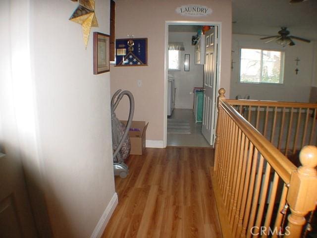 corridor with a healthy amount of sunlight, baseboards, wood finished floors, and an upstairs landing