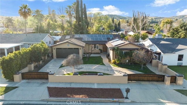 ranch-style house featuring an attached garage, a mountain view, solar panels, driveway, and a residential view