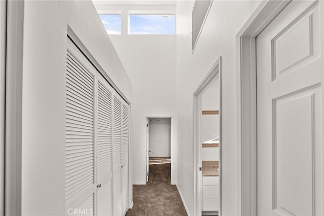 hall with baseboards, dark colored carpet, and a towering ceiling