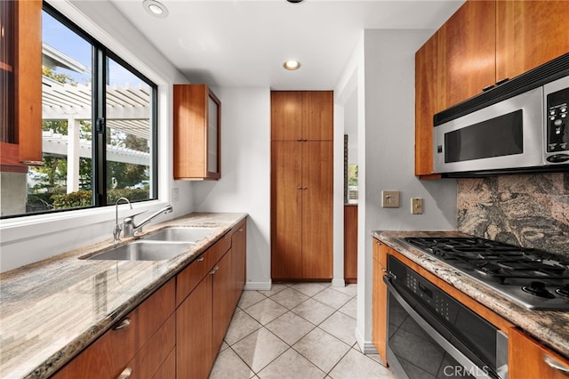 kitchen with brown cabinets, a sink, light stone counters, tasteful backsplash, and stainless steel appliances