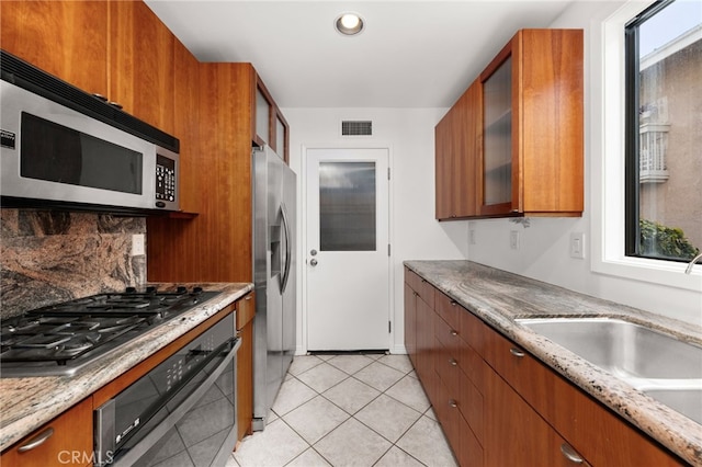 kitchen featuring visible vents, a sink, glass insert cabinets, appliances with stainless steel finishes, and brown cabinets