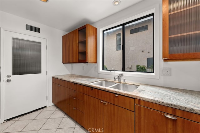 kitchen featuring light tile patterned floors, brown cabinets, glass insert cabinets, and a sink