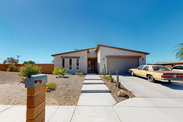 mid-century home featuring an attached garage, fence, concrete driveway, and stucco siding