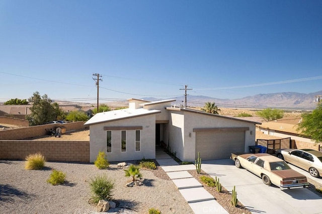 view of front of property with driveway, a garage, fence, a mountain view, and stucco siding