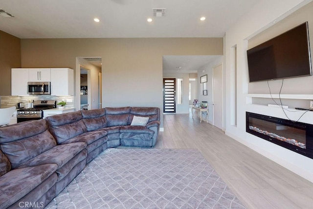 living area featuring a glass covered fireplace, visible vents, and recessed lighting