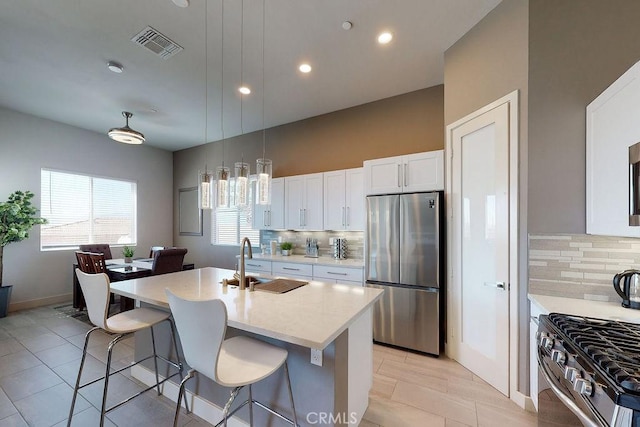 kitchen with stainless steel appliances, visible vents, white cabinetry, a sink, and a kitchen breakfast bar