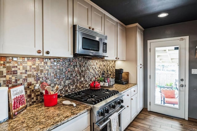 kitchen featuring white cabinets, appliances with stainless steel finishes, light wood-type flooring, decorative backsplash, and dark stone countertops