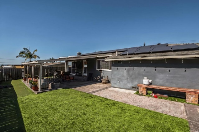 rear view of house with fence, a patio, a lawn, and solar panels