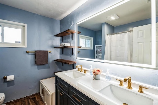 bathroom featuring wood finished floors, a sink, toilet, and double vanity