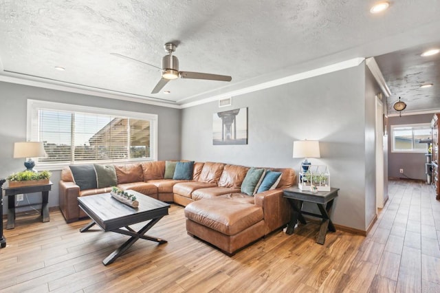 living room featuring light wood finished floors, a textured ceiling, visible vents, and crown molding