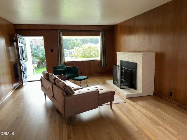 living area featuring light wood-style floors, a brick fireplace, wooden walls, and baseboards