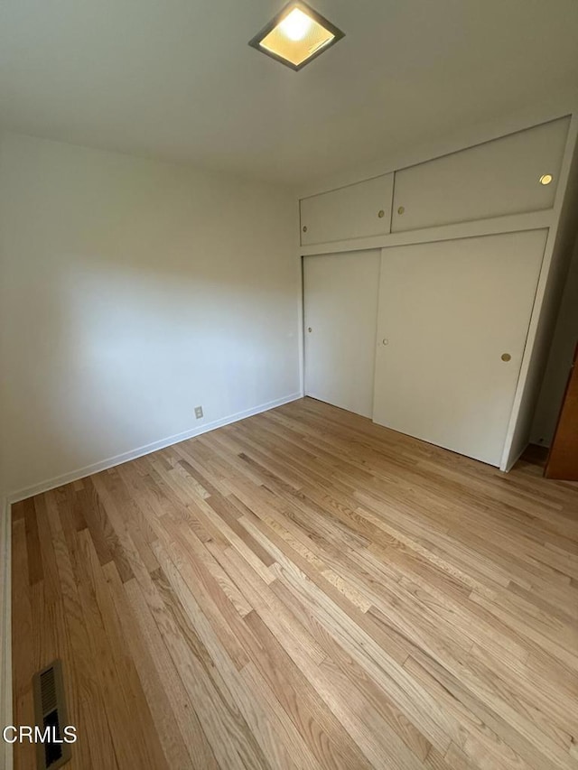 unfurnished bedroom featuring baseboards, a closet, visible vents, and light wood-style floors