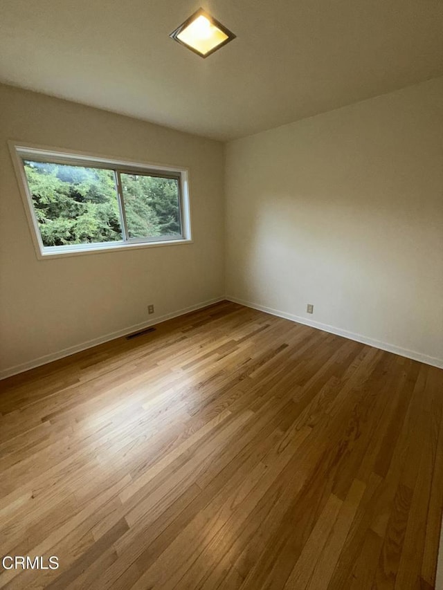 empty room featuring light wood finished floors, baseboards, and visible vents