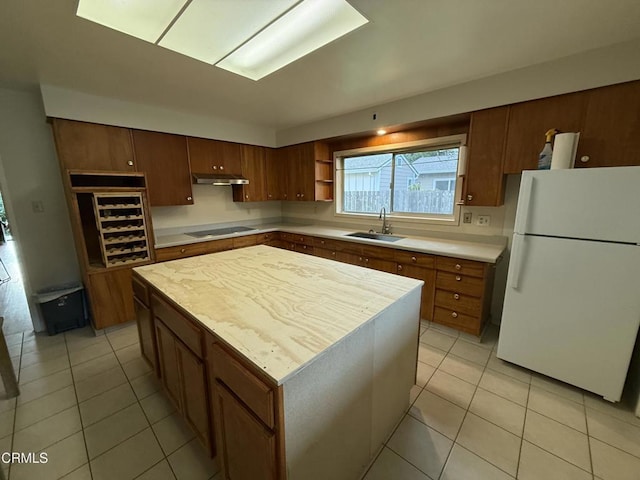 kitchen with under cabinet range hood, a sink, light countertops, freestanding refrigerator, and a center island