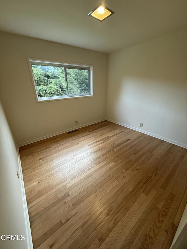 unfurnished room featuring light wood-type flooring, visible vents, and baseboards