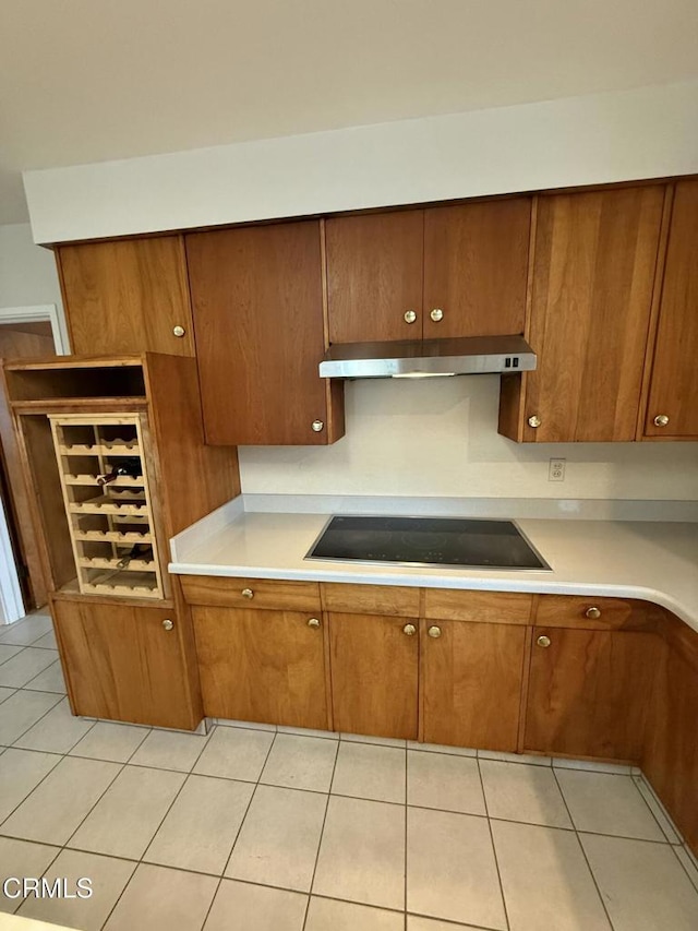 kitchen with light tile patterned flooring, black electric cooktop, under cabinet range hood, light countertops, and brown cabinetry