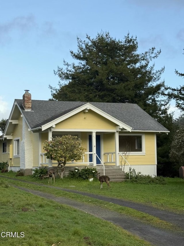 bungalow-style house with a shingled roof, a porch, a chimney, and a front lawn