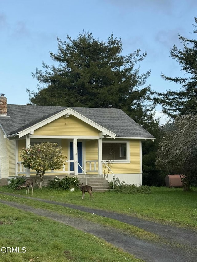 bungalow-style home featuring a porch, roof with shingles, a chimney, and a front yard