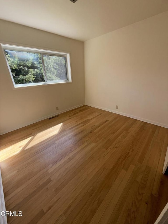 spare room with visible vents, baseboards, and wood finished floors