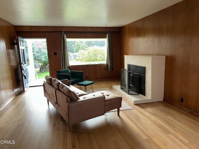 living room featuring light wood-style flooring, wooden walls, a fireplace, and baseboards