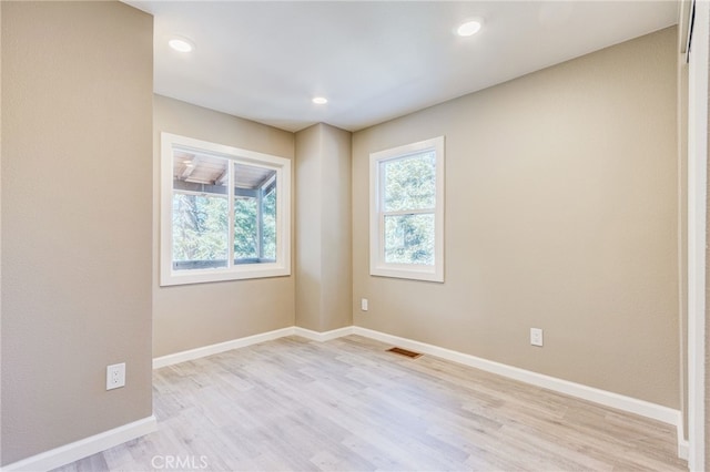 empty room featuring a healthy amount of sunlight, light wood-style floors, baseboards, and visible vents