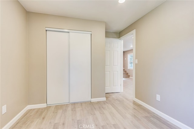 unfurnished bedroom with light wood-style flooring, baseboards, and a closet