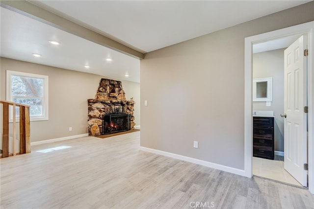 unfurnished living room featuring baseboards, a stone fireplace, recessed lighting, and light wood-style floors