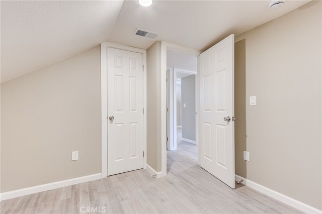 additional living space with baseboards, vaulted ceiling, visible vents, and light wood-style floors