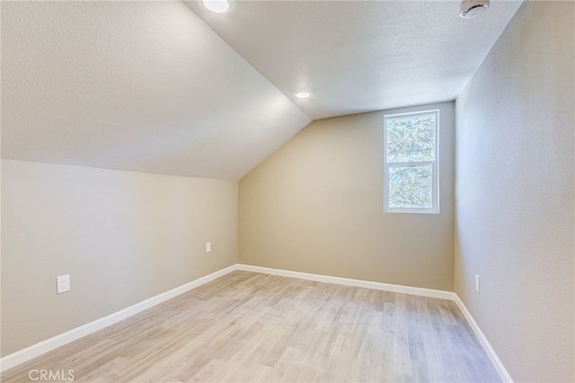 bonus room with lofted ceiling, baseboards, a textured ceiling, and light wood finished floors