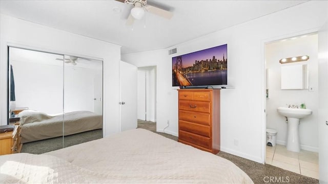 tiled bedroom with a ceiling fan, baseboards, a closet, carpet, and ensuite bath