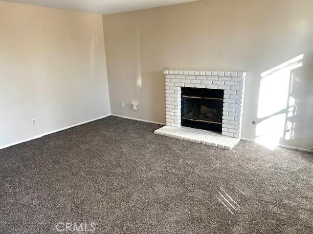 unfurnished living room featuring a brick fireplace and dark colored carpet