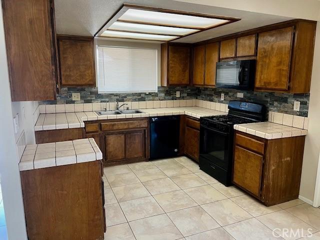 kitchen with tasteful backsplash, tile counters, dark brown cabinets, black appliances, and a sink