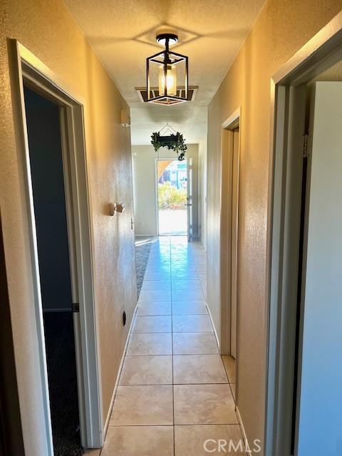 hall with light tile patterned floors, baseboards, a textured ceiling, and a textured wall