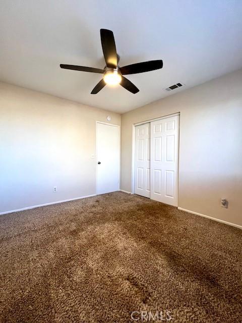 unfurnished bedroom featuring carpet floors, a ceiling fan, visible vents, and a closet