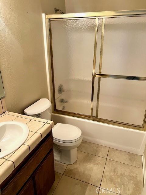 bathroom with tile patterned floors, vanity, toilet, and bath / shower combo with glass door