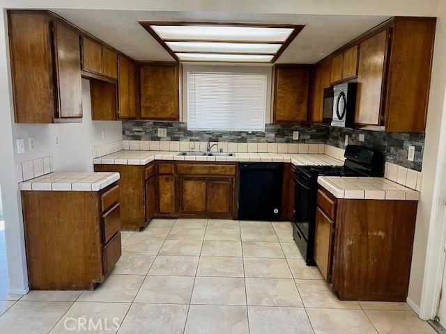 kitchen featuring tile countertops, light tile patterned flooring, a sink, black appliances, and tasteful backsplash