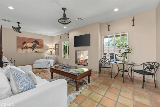 living room featuring a warm lit fireplace, baseboards, visible vents, and recessed lighting