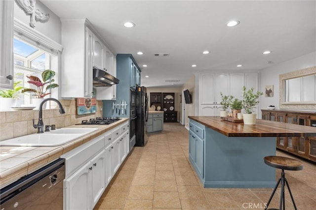 kitchen featuring butcher block countertops, under cabinet range hood, blue cabinetry, and black appliances